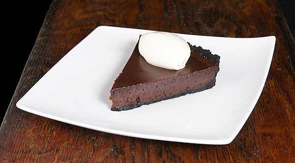 tarts recipes, tart recipes, chocolate truffle A photo of a chocolate truffle tart topped with a mascarpone cream quenelle on a white dish placed on a dark wooden board.