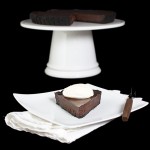 Oreo Chocolate Truffle Cake with Chocolate Glaze A photo of a Chocolate Truffle Tart with Chocolate Glaze displayed in the background on a white cake stand with a slice of Chocolate Truffle Tart on a white dessert dish placed in front of the cake stand.