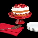 Strawberry and Cream Cake A photo of Strawberry and Cream Cake on a red cake stand displayed with white dessert dishes, red napkins and an antique silver cake lifter.