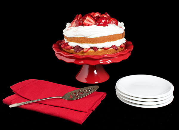 Strawberry and Cream Cake A photo of Strawberry and Cream Cake on a red cake stand displayed with white dessert dishes, red napkins and an antique silver cake lifter.