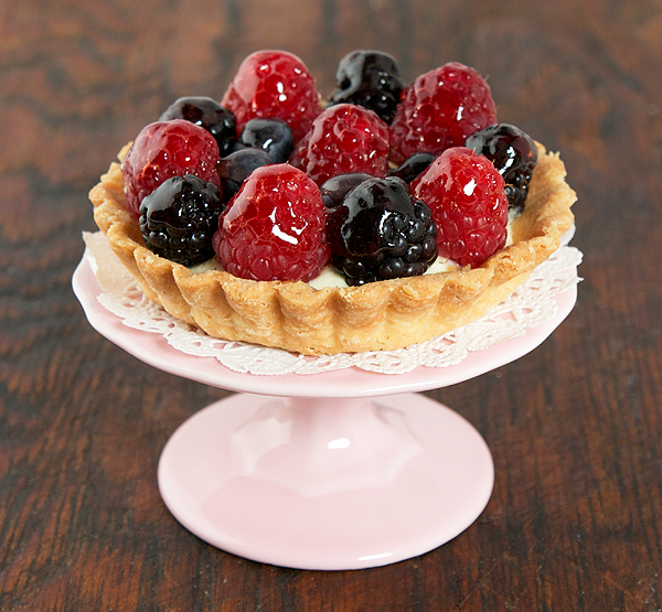 Fruit Tart A close up photo of a mini fruit tart displayed on a pink cupcake stand.