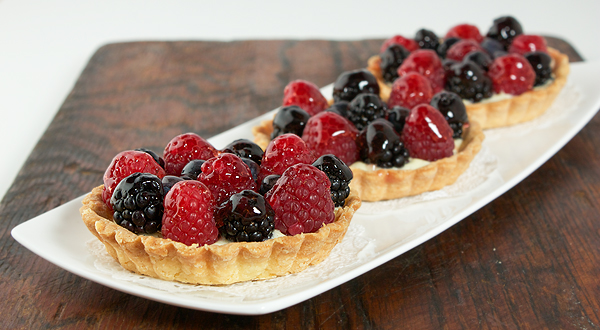 Fruit Tarts A photo of three small Fruit Tarts placed in a row and displayed on a white rectangular dish.