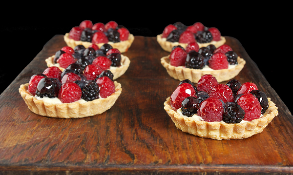 Mini Fruit Tarts A photo of six Mini Fruit Tarts displayed on a dark wooden board.