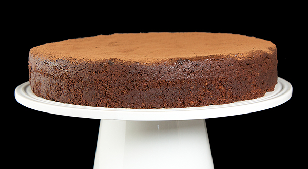 Torta Caprese - Flourless Chocolate Torte A photo of a Torta Caprese, Italian Flourless Chocolate Torte dusted with cocoa powder and displayed on a white cake stand.