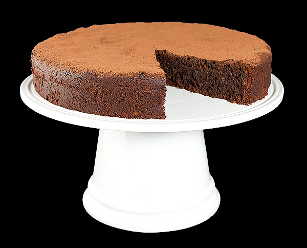 chocolate cake recipes, moist chocolate cake, easy chocolate cake recipe, italian cakes A photo of an Italian Flourless Chocolate Cake, Torta Caprese with a slice removed displayed on a white cake stand.