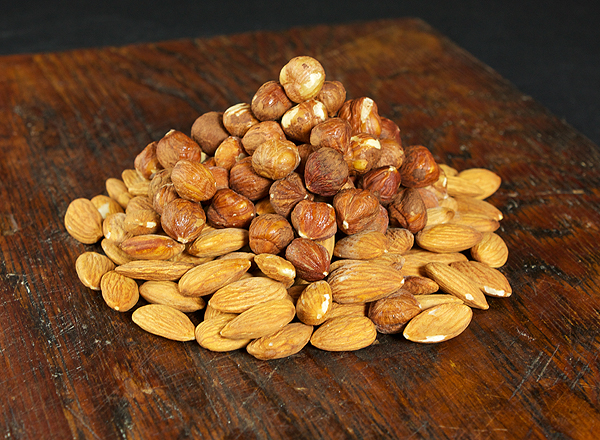 Almonds and Hazelnuts A photo of Almonds and Hazelnuts displayed in a heap on a dark wooden board for use in Torta Caprese, Italian Chocolate Cake.