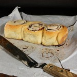 Cinnamon Rolls A photo of 3 Cinnamon Rolls fresh out of the oven on non-stick baking paper with an offset spatula off to the side.