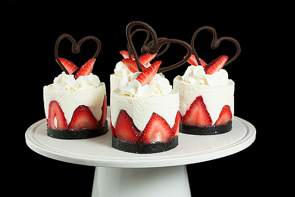 Italian Cake A photo of an Italian Cake, Torta di Fragole e Crema Soffice di Yogurt, in mini form, garnished with fresh strawberries and a chocolate heart displayed on a white cake stand.