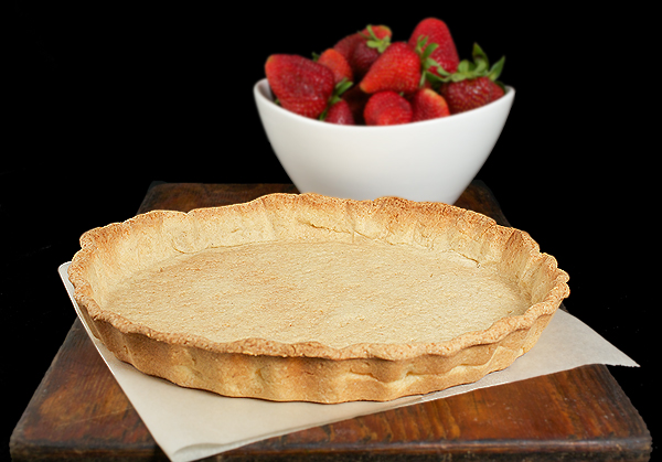 Pasta Frolla Tart Shell & Fresh Strawberries A photo of a baked Pasta Frolla tart shell and a bowl of fresh strawberries on a dark wooden board.