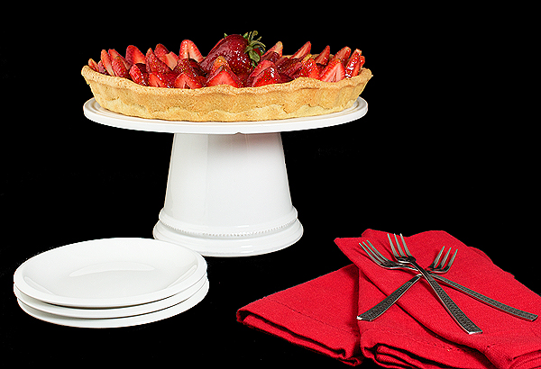 Strawberry Tart A photo of a Strawberry Tart with Pastry Cream lightened with Whipped Cream and topped with fresh Strawberries and coated with a thin layer of Apricot Glaze, displayed on a white cake stand with dessert dishes, dessert forks and red napkins.
