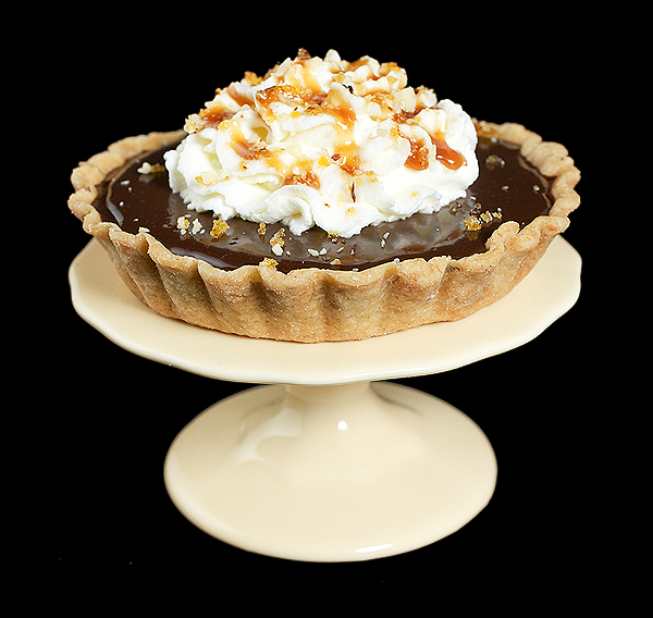 Caramel Recipe A photo of a Chocolate-Caramel Tart with sweetened whipped cream, caramel sauce and hazelnut praline displayed on a yellow cupcake stand.