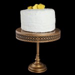 Grace's Sweet Life Coconut Cake A photo of a Coconut Cake layered with Mango Curd and 7-Minute Frosting and decorated with fluffy White Frosting, finely grated white chocolate and mango hearts displayed on a tall, gold cake stand.