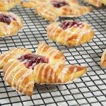 Grace's Sweet Life Cherry Danish A photo of Cherry Danishes drizzled with icing cooling on a wire rack.