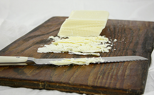 Grace's Sweet Life White Chocolate Vanilla Bean Pudding Mise en Place Vanilla Bean Pudding mise en place, block of white chocolate, displayed on a dark wooden board with serrated knife.