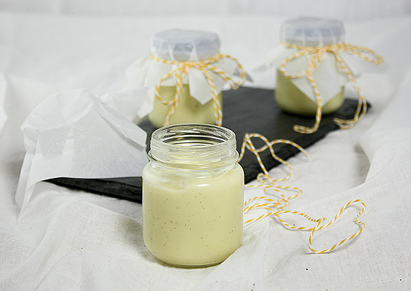 White Chocolate Vanilla Bean Pudding from Grace's Sweet Life A photo of White Chocolate Vanilla Bean Pudding displayed in glass jars topped with non-stick baking paper squares secured with orange and white string.
