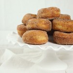 A picture of Potato Zeppole rolled in cinnamon sugar displayed on a white cake stand.