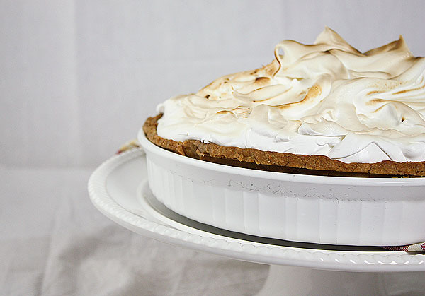 A close up cropped photo showing one-half of a Lemon Meringue Tart displayed in white tart dish on white cake stand.