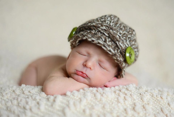 A photo of Grace's great-nephew, Grayson. wearing nothing but a grey wool cap with green button on a cream colour blanket.
