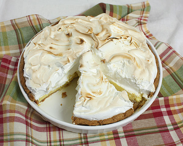 A photo taken looking down on Lemon Meringue Tart with one slice removed displayed on a multi coloured cloth napkin.