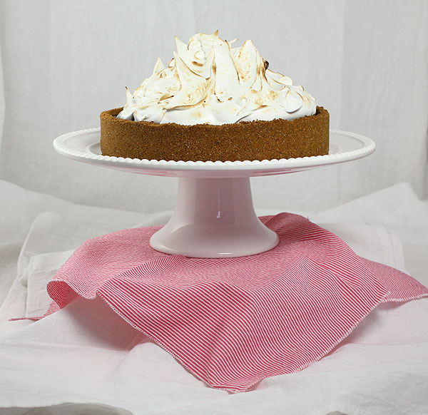 A photo of S mores Pie on white cake stand displayed on pink and white striped cloth napkin.