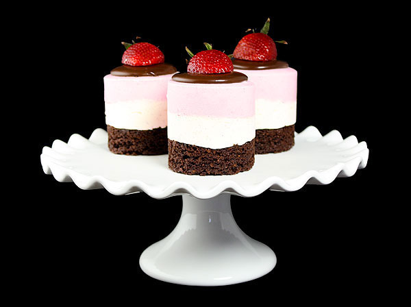 A photo of three Mini Neapolitan Mousse Cakes garnished with fresh strawberries displayed on white cake stand.