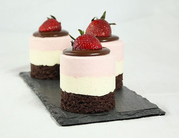 Photo of three Neapolitan Layer Mousse Cakes displayed in a row on black slate board.