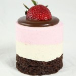 A close up photo of a Neapolitan Mousse Cake garnished with Dark Chocolate Ganache and fresh strawberry.