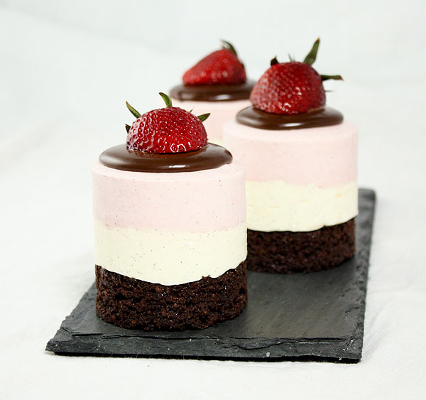 A photo of three Neapolitan Mousse Cakes arranged in a row, one behind the other, on a rectangle shaped slate board.