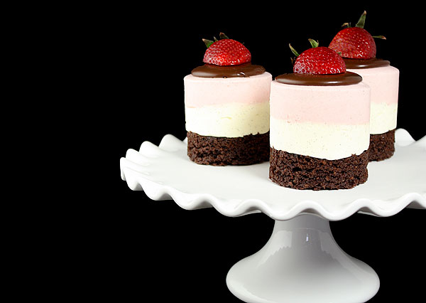 A cropped photo of three Neapolitan Mousse Cakes displayed on a white cake stand.