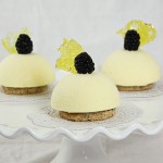 Photo of three Honey-Lemon Semifreddo desserts garnished with fresh blackberries and Limoncello bubble sugar displayed on white cake stand.