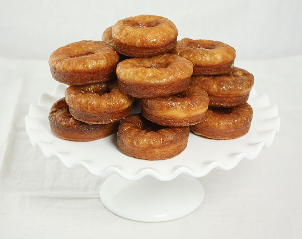 Photo taken looking down Vanilla Bean Cream Filled Croissant Doughnuts stacked on a white cake stand.
