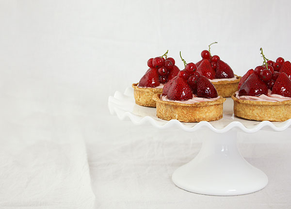 Close up cropped photo of Berry Cheesecake Tarts displayed on white cake stand.