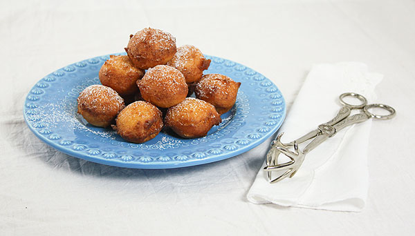 Photo of blue dessert dish piled high with Frittelle di Ricotta, Italian Sweet Ricotta Fritters with antique serving tongs.