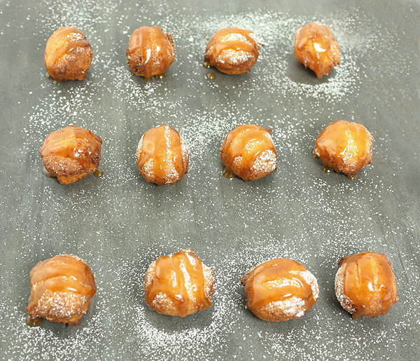 Close up photo taken looking down on rows of Sweet Ricotta Fritters drizzled with Butter-Rum Caramel Sauce.