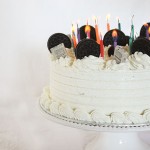 A cropped photo showing one half of an Oreo Cookies and Cream Ice Cream Cake decorated with Oreo Cookies, Mini Cookies and Cream Chocolate Bars and birthday candles.