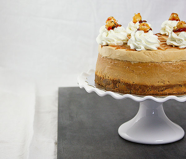 Close up cropped photo of Dulce de Leche Cheesecake decorated with swirls of whipped cream and garnished with Hazelnut Praline.