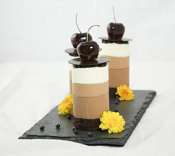 Mini Chocolate Mousse Cakes displayed in a row, one behind the other, on black slate with yellow edible flowers and Callebaut Crispearls.