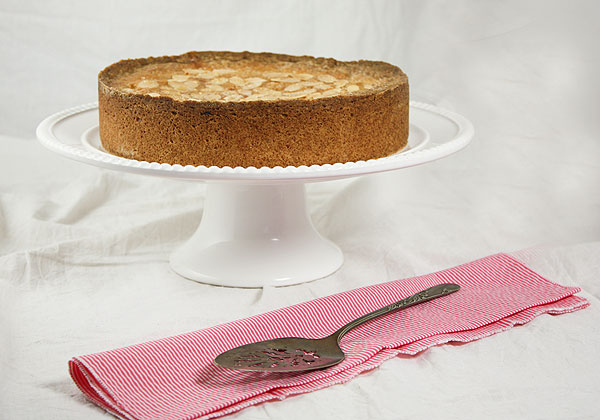 Photo of Blackberry and Almond Shortbread Cake displayed on white ruffled edge cake stand with pink and white striped cloth napkin and antique cake server.