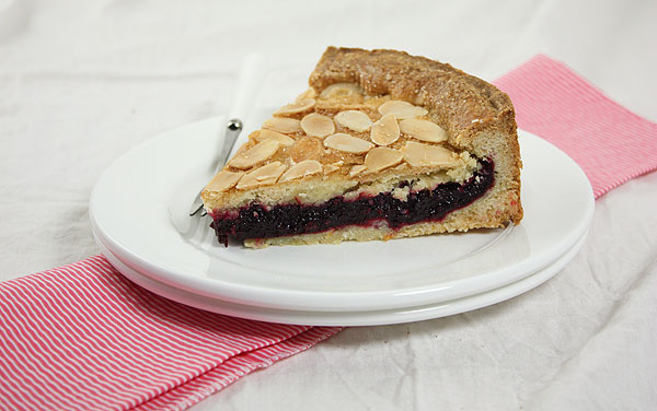Close up photo of a slice of Blackberry Shortbread Cake displayed on double stack of white dessert dishes on pink and white striped cloth napkin.